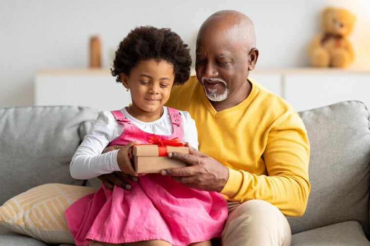 african american girl being handed a gift by her grandfather