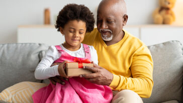 african american girl being handed a gift by her grandfather