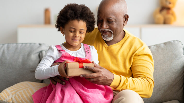 african american girl being handed a gift by her grandfather
